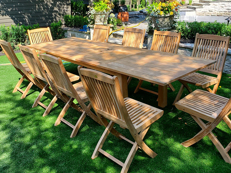 Long rectangular teak dining table surrounded by armless folding chairs