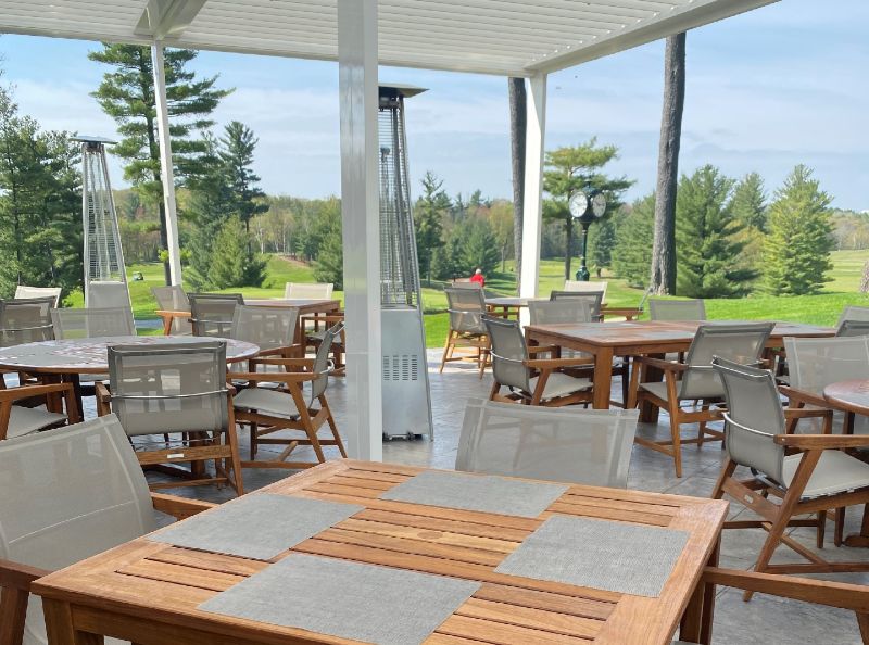Square and round teak tables with silver sling chairs under a white canopy at Beacon Hall Golf Club overlooking the course